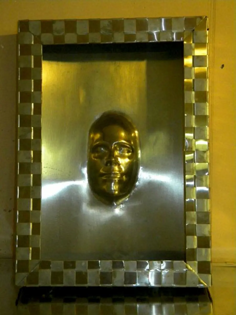 Gesichtsrelief aus Metall in gemustertem Rahmen