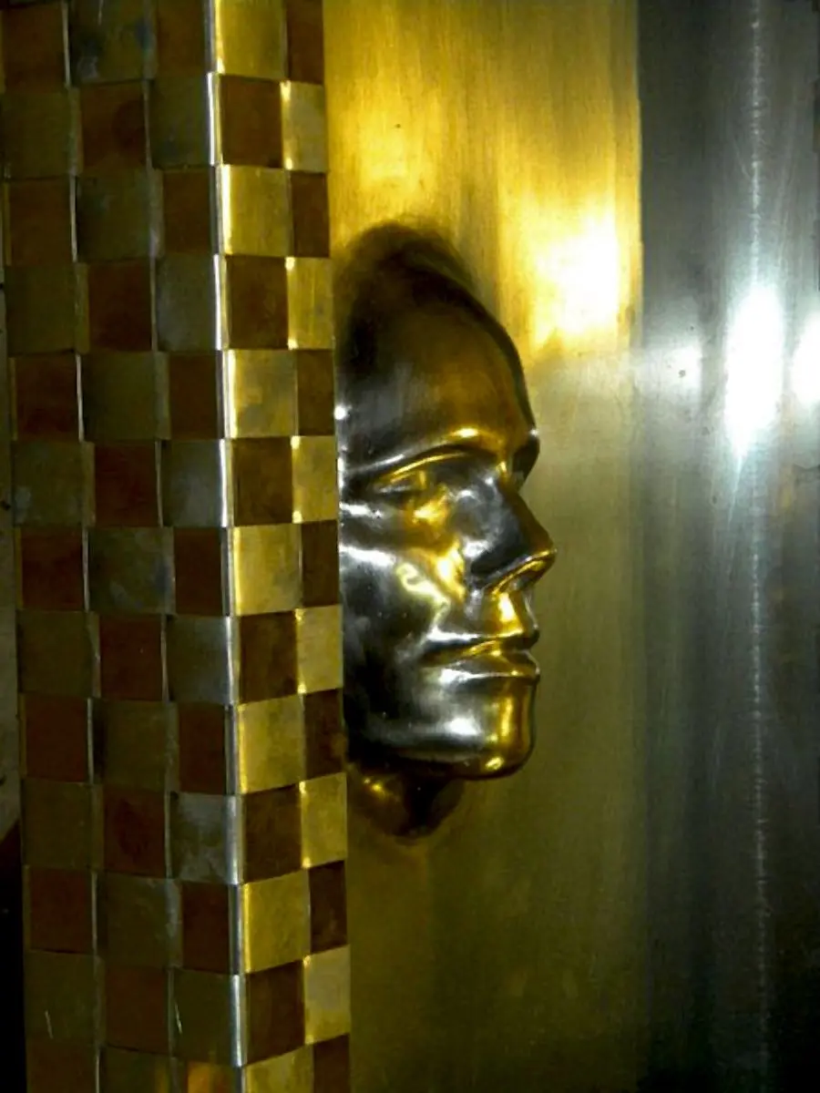 Gesichtsrelief an einer Metallsäule mit Karomuster