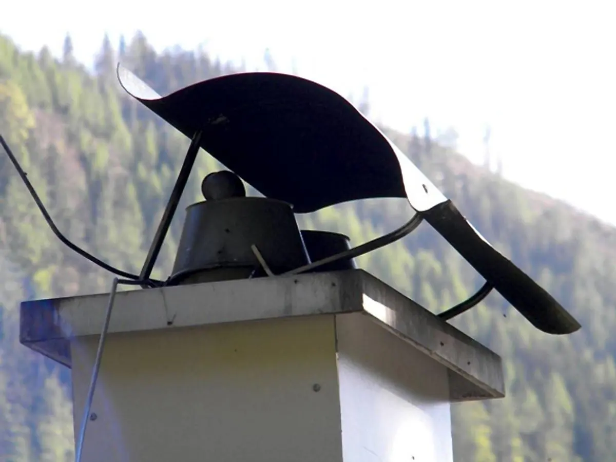Kaminabdeckung aus Blech vor bewaldetem Hang